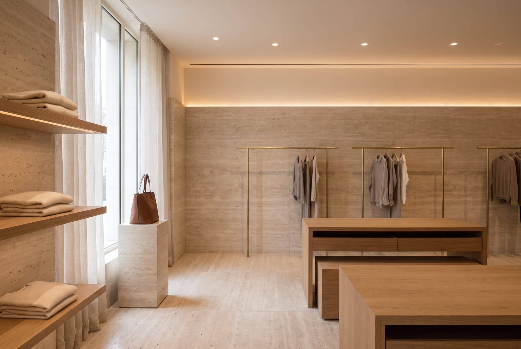 A boutique interior in warm travertine with oak display tables and brass rails